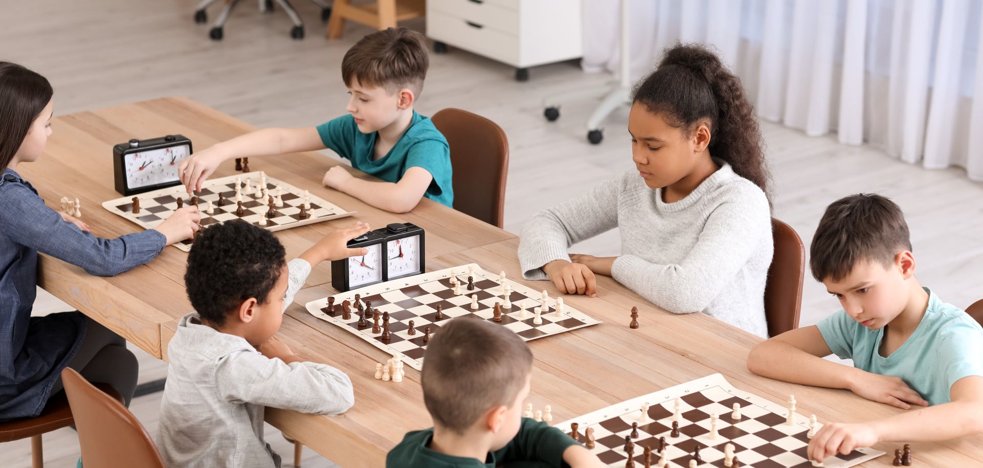 Elementary school students play three games of chess sitting at a wooden table with their school teacher in Los Angeles.